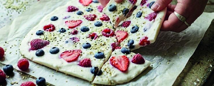 Frozen yoghurt bark studded with strawberries and blueberries, being broken into shards.